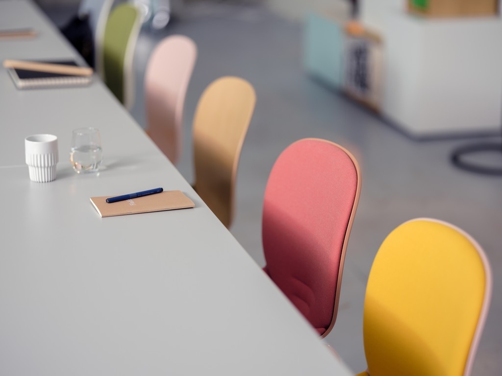 Pastel coloured RBM Noor chairs arranged in a row in a classroom with a pad and pencil, coffee cup and water glass on a table.