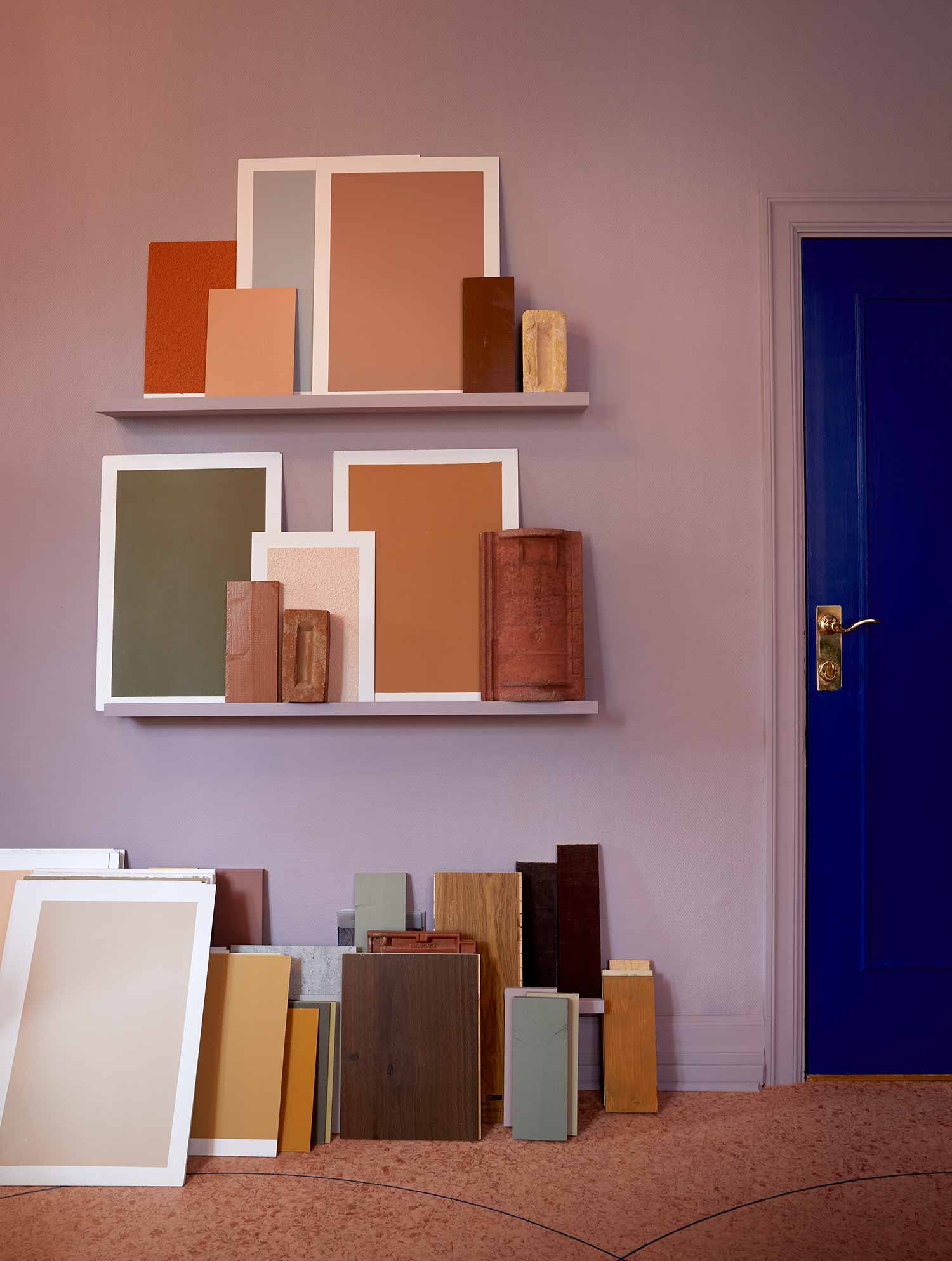 selection of paint colour cards on the floor and in frames on wall shelves with a blue door on the right