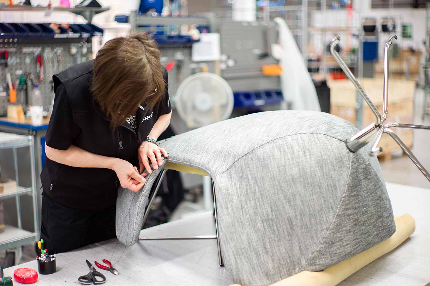 factory worker sewing offecct furniture grey material in flokk factory in tibro, sweden