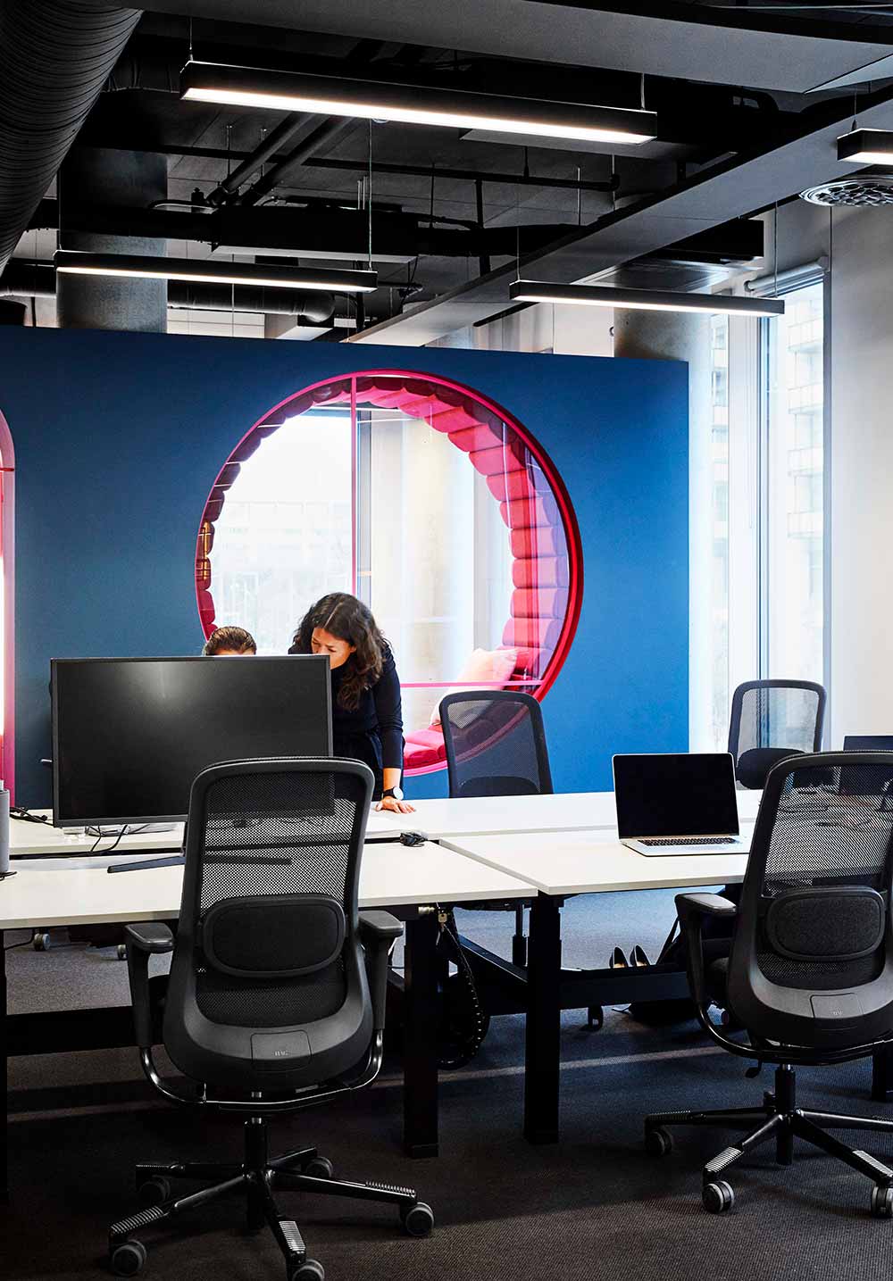 office design with black HÅG SoFi chairs and a blue wall in the background with a pink hole-shaped chair in the wall.