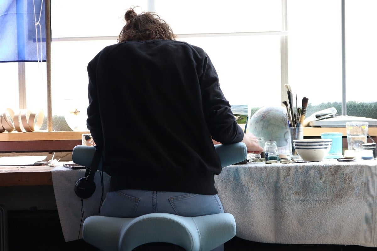 globe painter sitting backwards on a HÅG Capisco concentrating at her workbench
